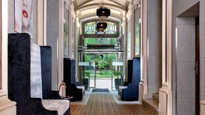 A grand hallway with a patterned carpet, seating areas with dark upholstery, and a view of greenery outside. - Leonardo Boutique Hotel Krakow Old Town (Kraków)