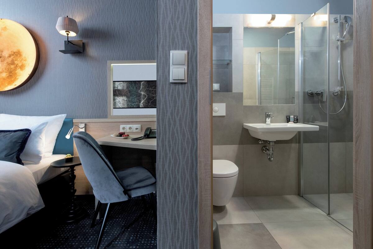 Une chambre d’hôtel comprenant un lit, un bureau, une chaise et une salle de bain avec douche, lavabo et toilettes.