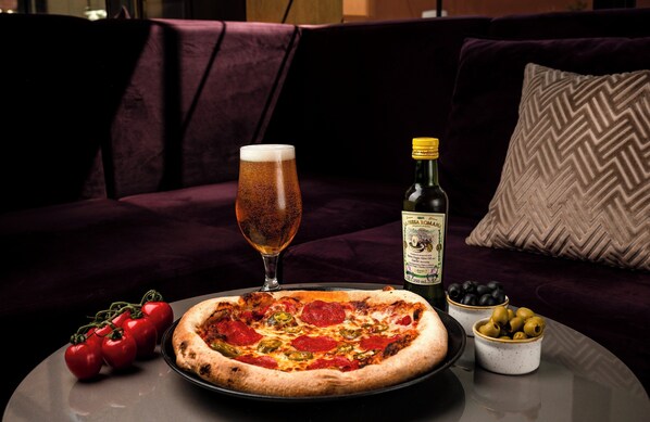 Une pizza sur une table, accompagnée d’un verre de bière et d’une bouteille d’huile d’olive.