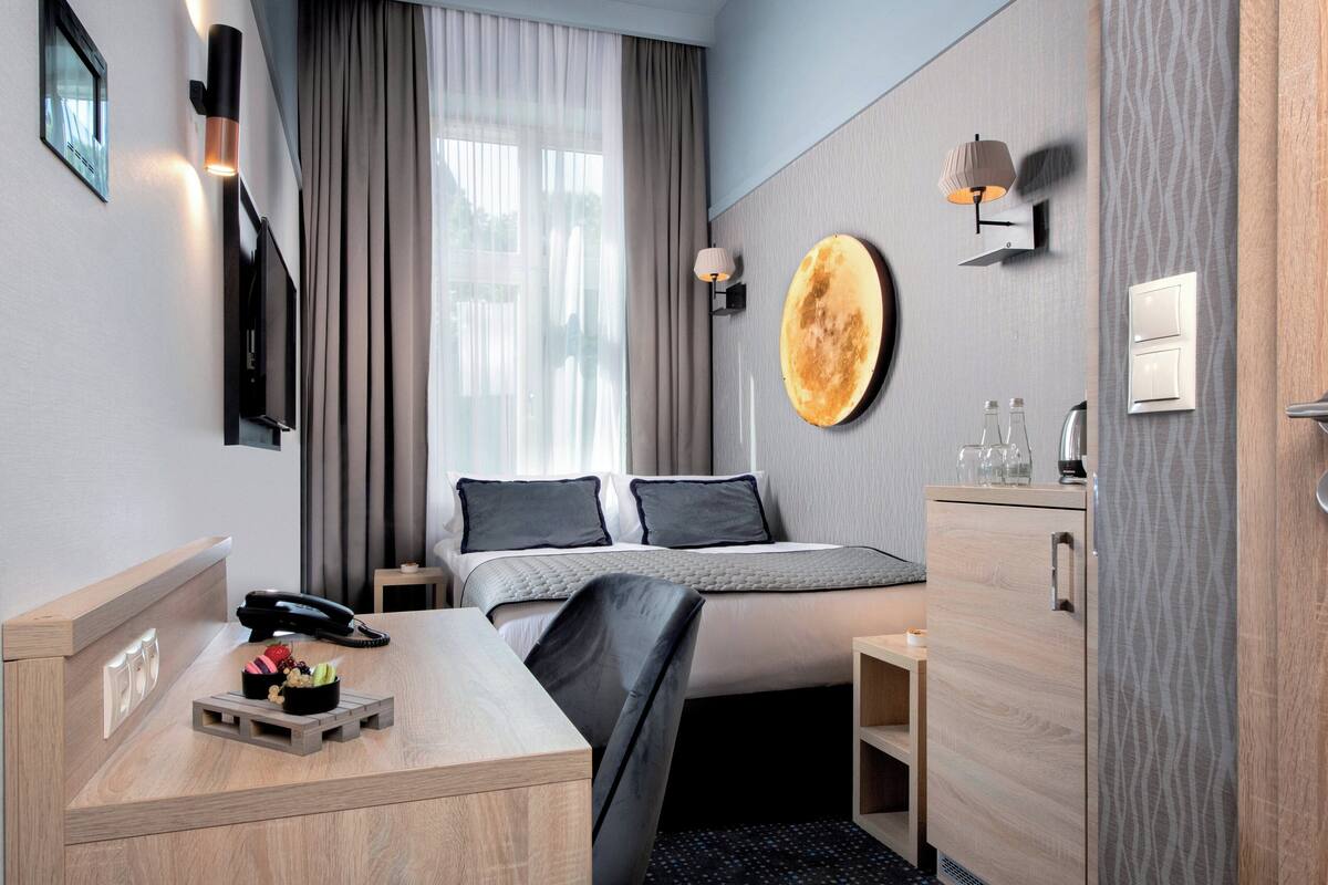 Une chambre d’hôtel moderne équipée d’un lit, d’une table de chevet, d’une lampe et d’un grand miroir rond fixé au mur.