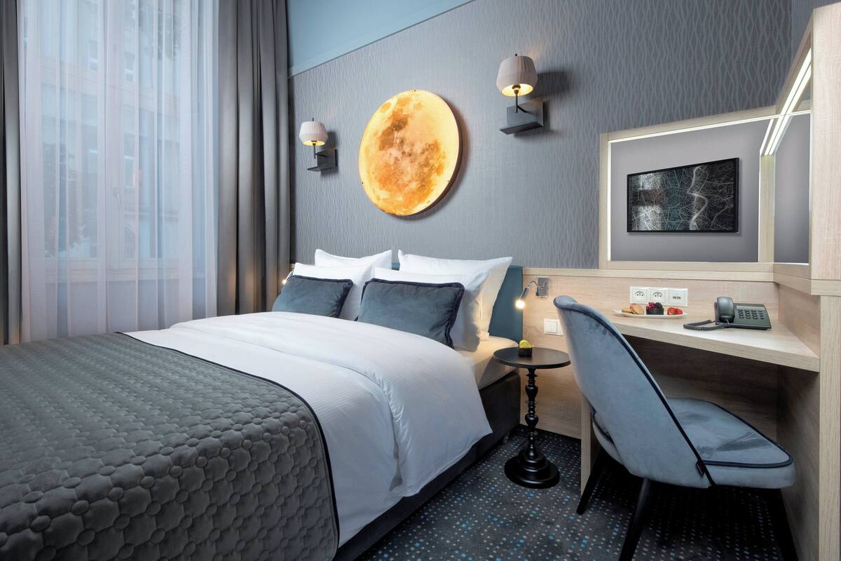 Une chambre d’hôtel avec un lit, un bureau, une chaise, un élément de décoration circulaire fixé au mur et un tableau encadré accroché au mur.