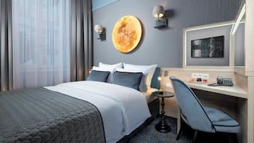 A hotel room with a bed, a desk, a chair, a wall-mounted lamp, and a large circular artwork.