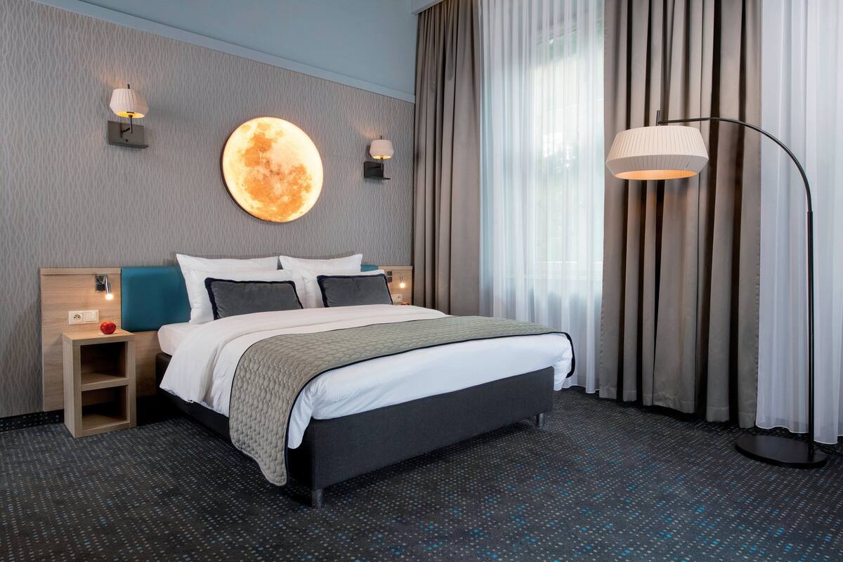 A modern hotel room with a large bed, two bedside tables, a floor lamp, and a wall-mounted lamp.