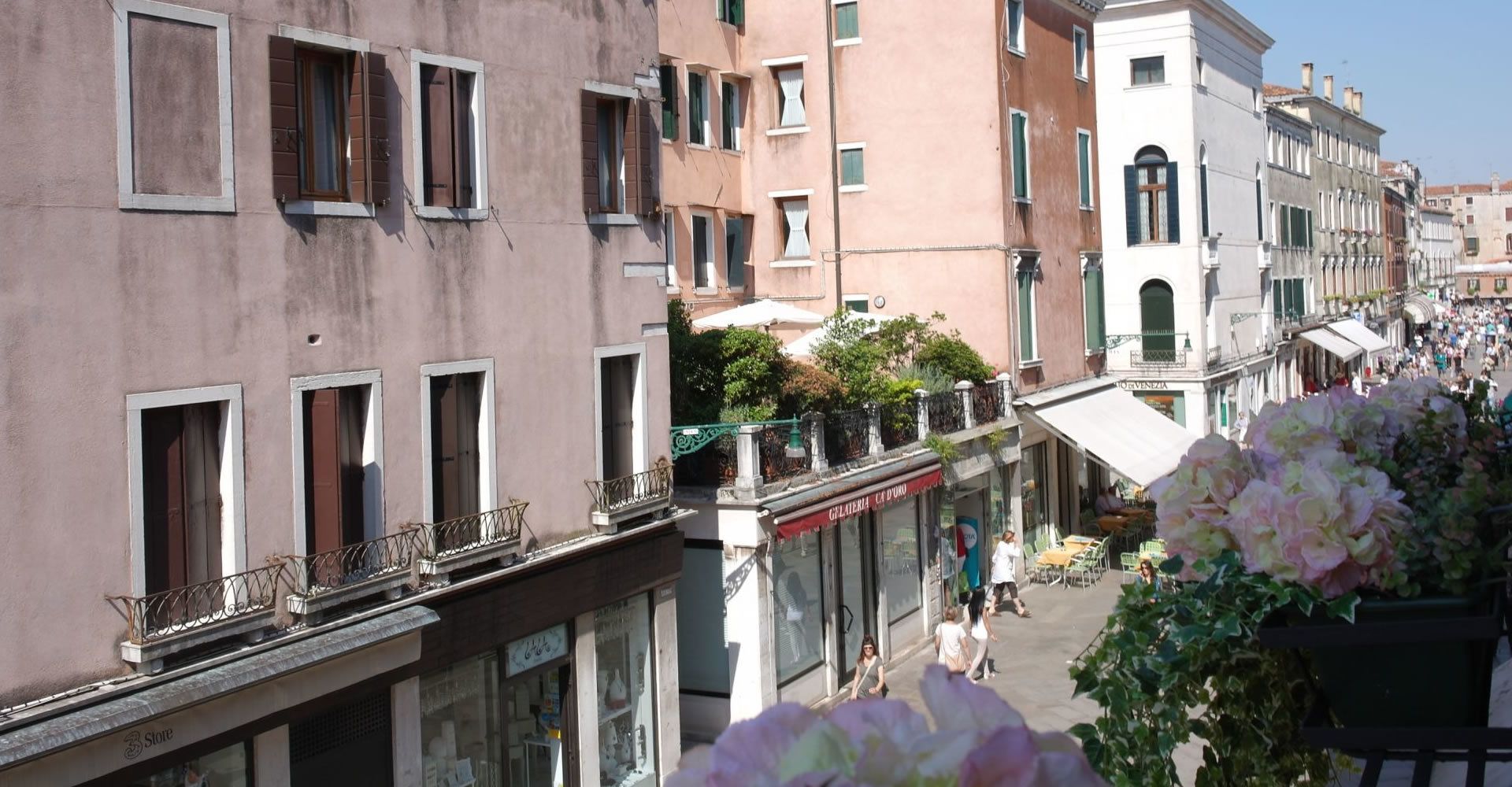 A narrow street lined with multi-story buildings, featuring balconies with metal railings and awnings over storefronts.