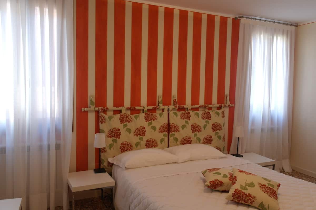 A bedroom with a striped wall, a bed with white bedding, two bedside tables, and a lamp on one table.