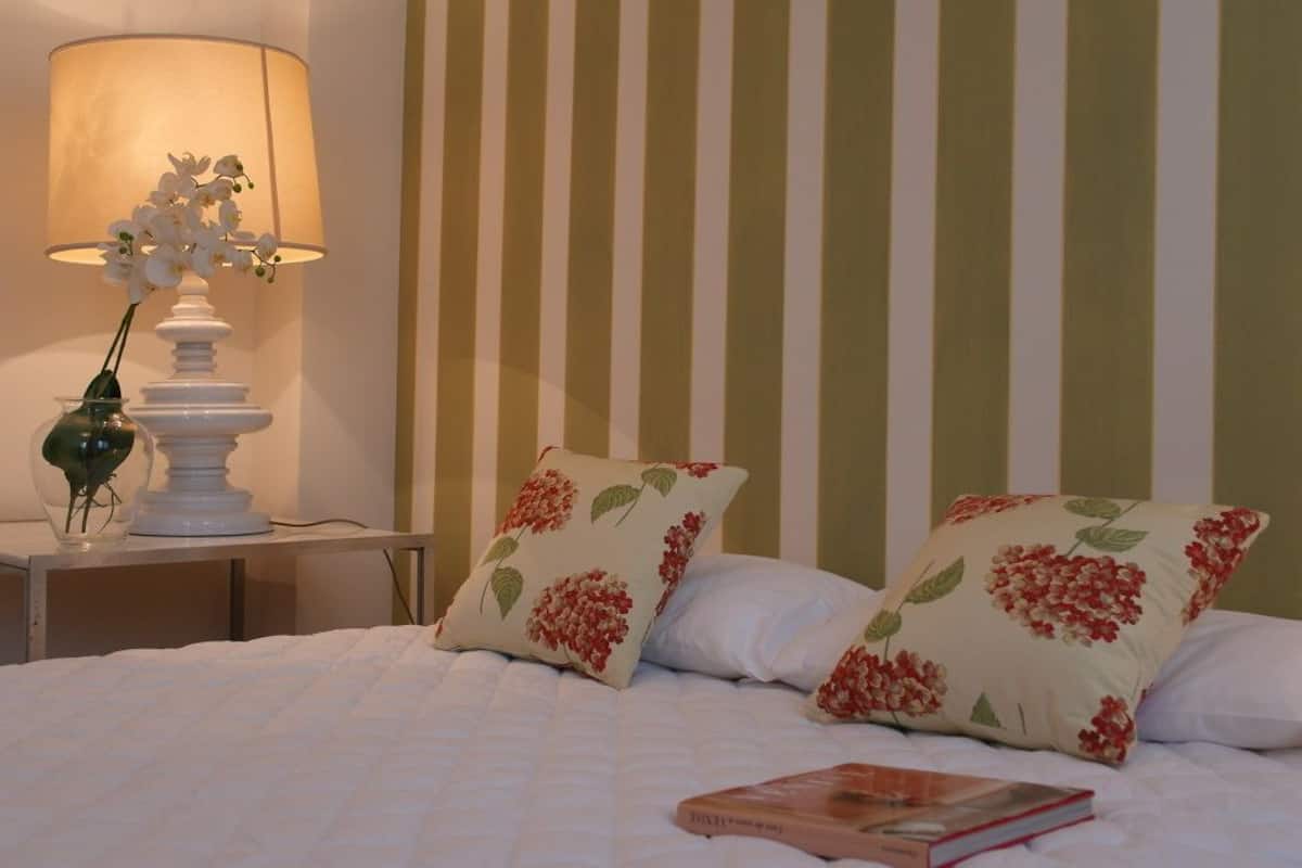 A neatly made bed with floral pillows, a bedside table with a lamp, and a book on the bed.
