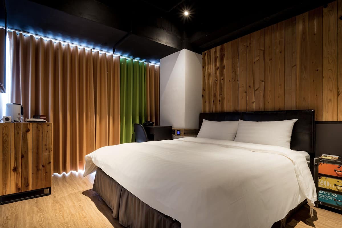 A modern hotel room with a large bed, wooden panel walls, a desk, and a wardrobe.