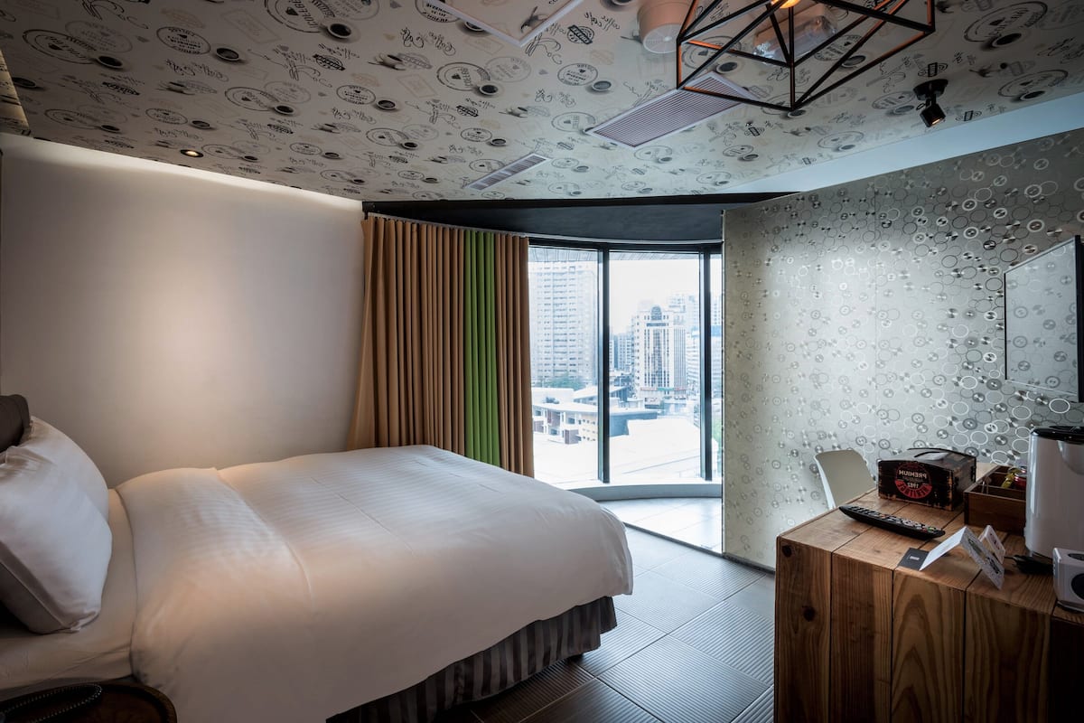 A modern hotel room with a large bed, a wooden desk, and a city view through the window.