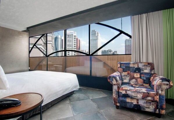 A hotel room with a bed, a patterned armchair, a small table, and a large window with a city view. - Calligraphy Greenway Hotel (Taichung)