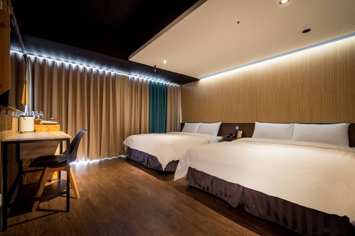 A hotel room with two beds, a desk with a chair, and a large window with curtains.