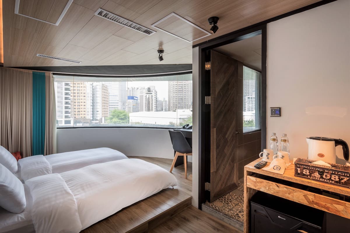 A hotel room with a bed, a desk, a chair, a coffee maker, and a view of the city.