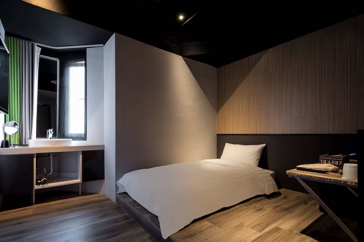 A modern bedroom with a bed, a desk with a mirror, and a window.