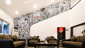 Un salon moderne agr émenté d’une œuvre d’art murale abstraite aux motifs géométriques en noir et blanc, de deux canapés, d’une table basse et d’un lampadaire rouge.