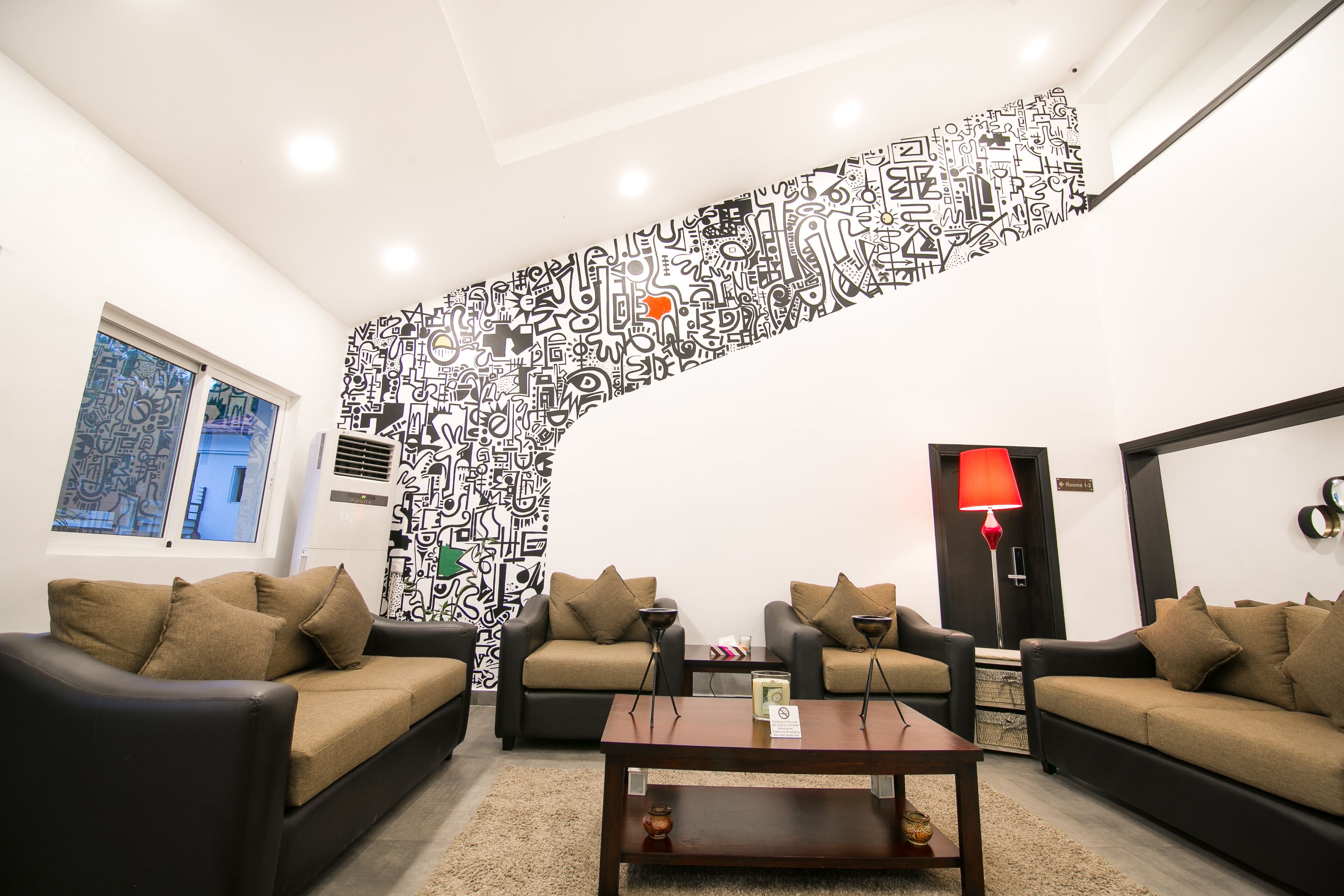 A modern living room with two sofas, a coffee table, and a red floor lamp. A unique black and white abstract mural decorates the wall.