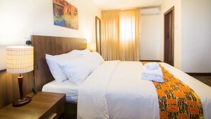 Une chambre d’hôtel avec un lit, une table de chevet, une lampe, un tableau et une fenêtre avec des rideaux.