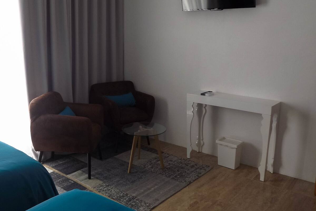 A hotel room with a bed, a chair, a small table, a TV, and a desk.