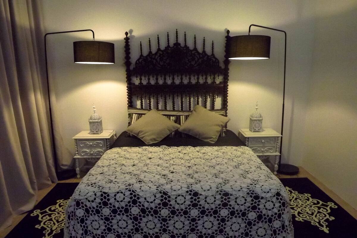 A neatly made bed with a patterned bedspread, two bedside lamps, and a decorative headboard.