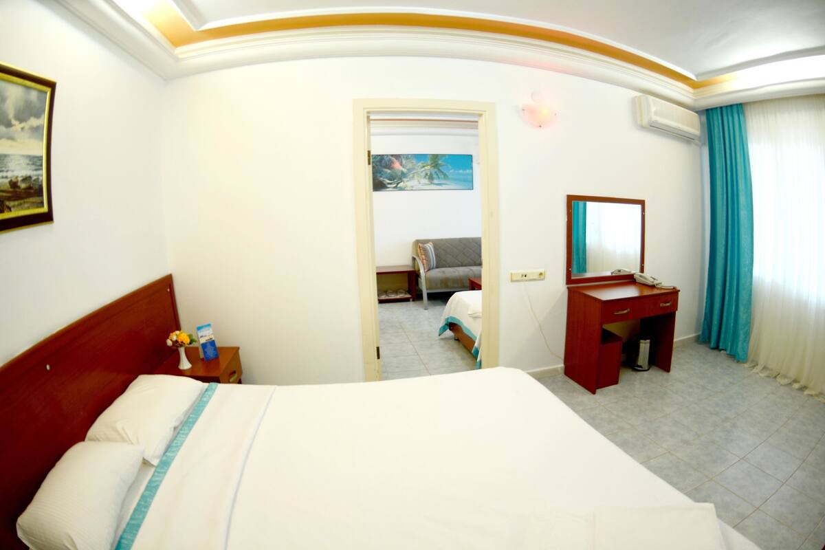 A hotel room with a bed, a desk, a chair, a painting, and a window with curtains.