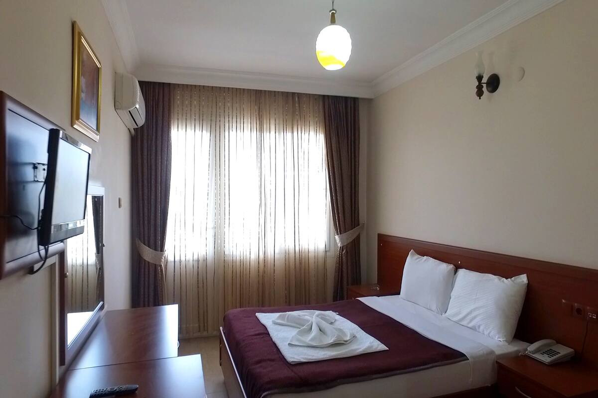 A hotel room with a bed, bedside table, TV, and curtains.
