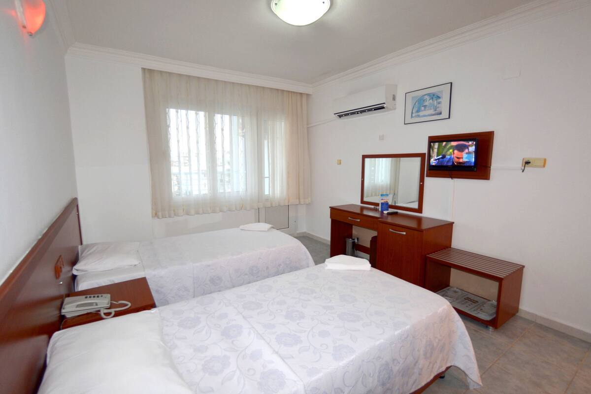 A hotel room with two single beds, a wooden dresser, a television, and a window with curtains.