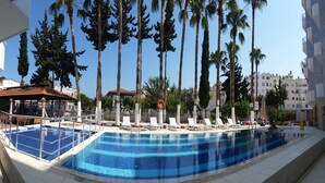 A swimming pool with lounge chairs, palm trees, and a building in the background. - Eylul Hotel (Erdemli)