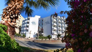 A hotel with multiple balconies, a central entrance, and a palm tree in the foreground. - Eylul Hotel (Erdemli)