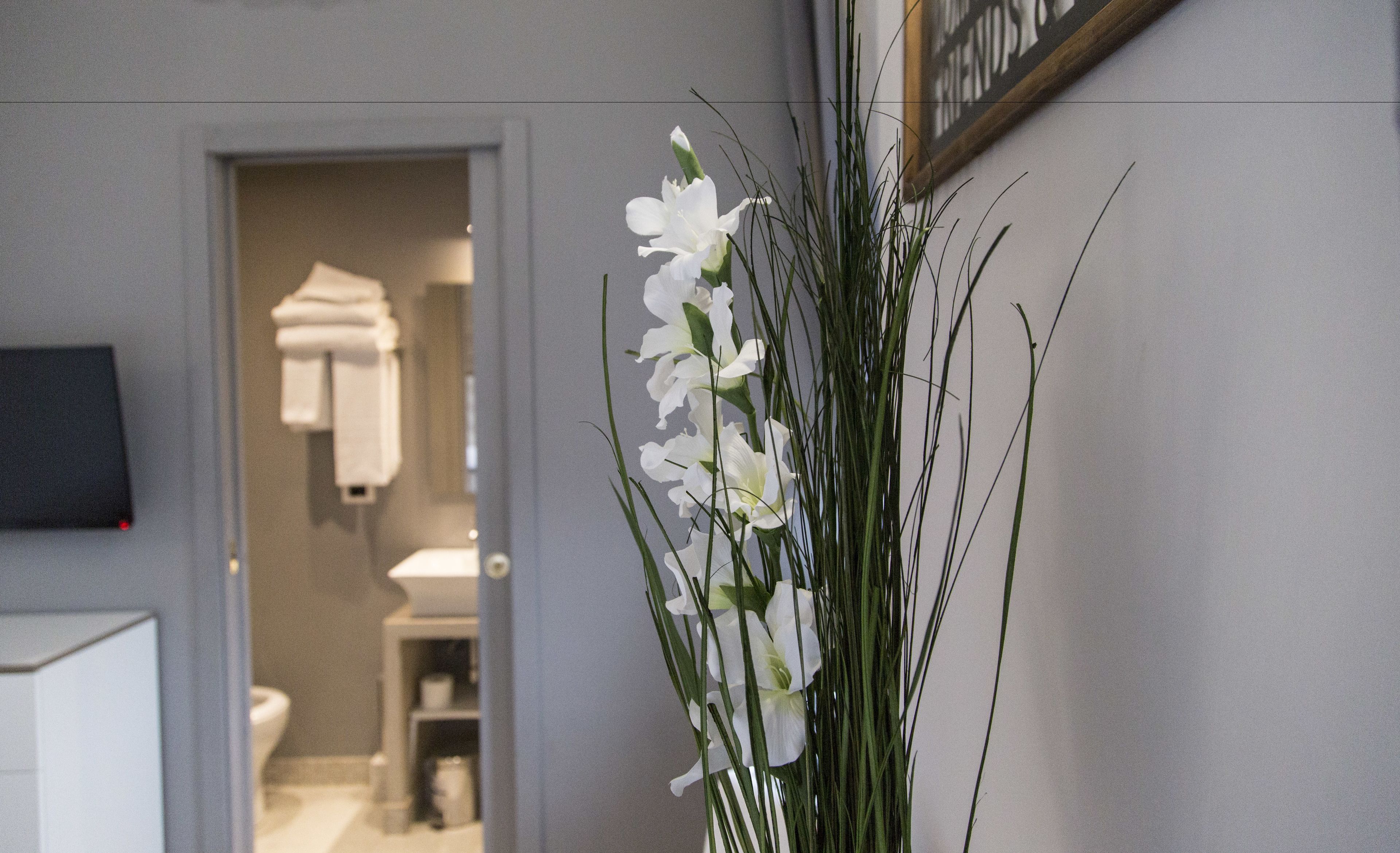 A hallway with a white flower arrangement, a door leading to a bathroom, and a framed picture on the wall.