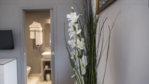 A hallway with a white flower arrangement, a door leading to a bathroom, and a framed picture on the wall. - Corso Experience (Rome)