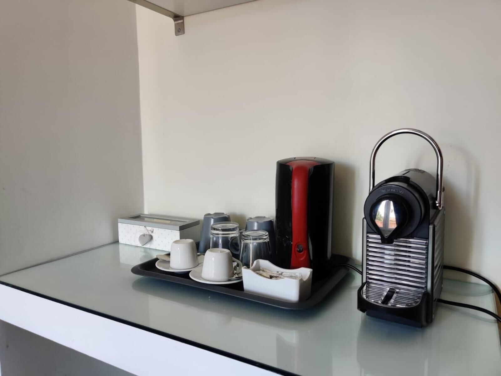 A glass coffee table with a tray holding a coffee maker, cups, and a box.