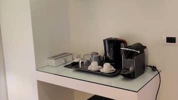 A compact kitchenette with a coffee machine, cups, and a small trash bin.
