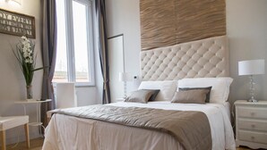 A modern bedroom with a large bed, a bedside table, a nightstand, a wall-mounted lamp, and a window with curtains. - Corso Experience (Rome)
