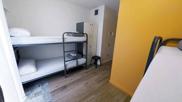 A bunk bed room with a wardrobe, a small stool, and a bed with a pillow.
