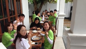 A group of people seated around a table in an outdoor dining area with white pillars and a tiled floor.