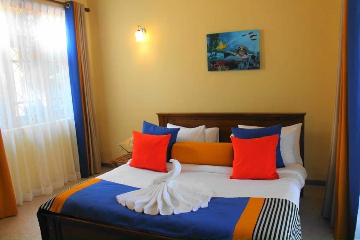 A hotel room with a bed, curtains, a painting, and a wall-mounted light.
