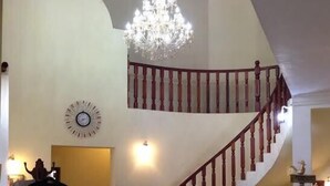 A staircase with wooden balusters, a chandelier, a clock, and a reception desk.