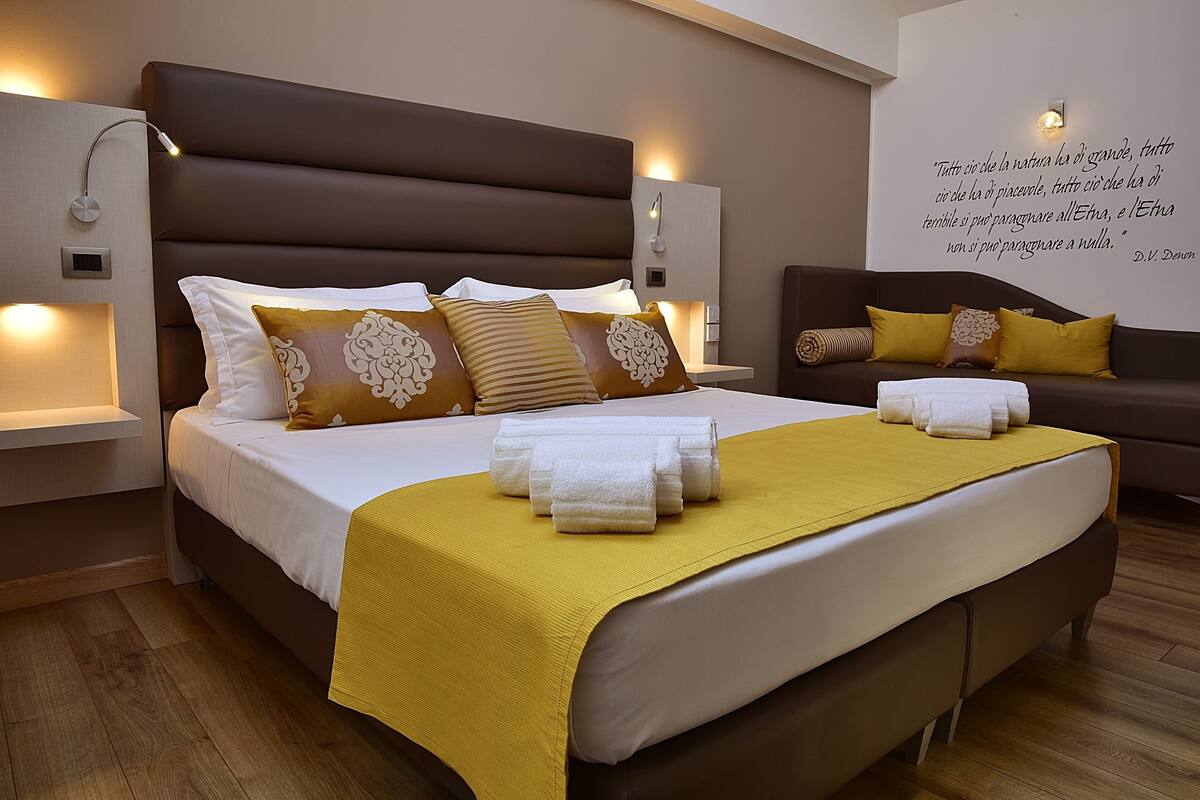 A modern hotel room with a large bed, a sofa, and a wall with a quote.