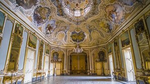 Una habitación ornamentada con un techo alto, elaborados frescos y una lámpara de araña.
