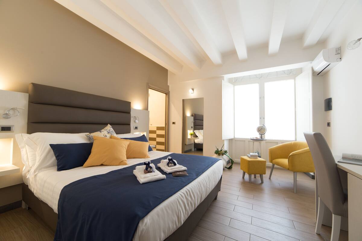 A modern hotel room with a large bed, a desk, and a chair.