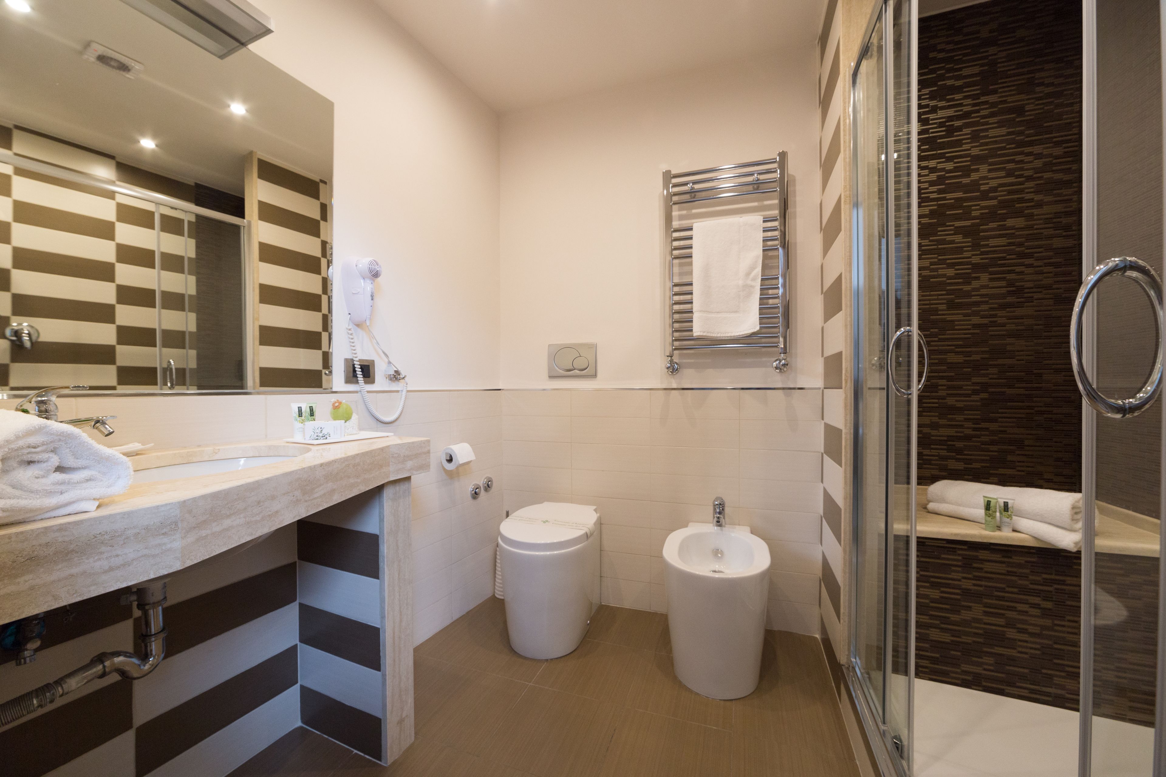 A modern bathroom with a large mirror, a sink, a bidet, and a glass-enclosed shower.