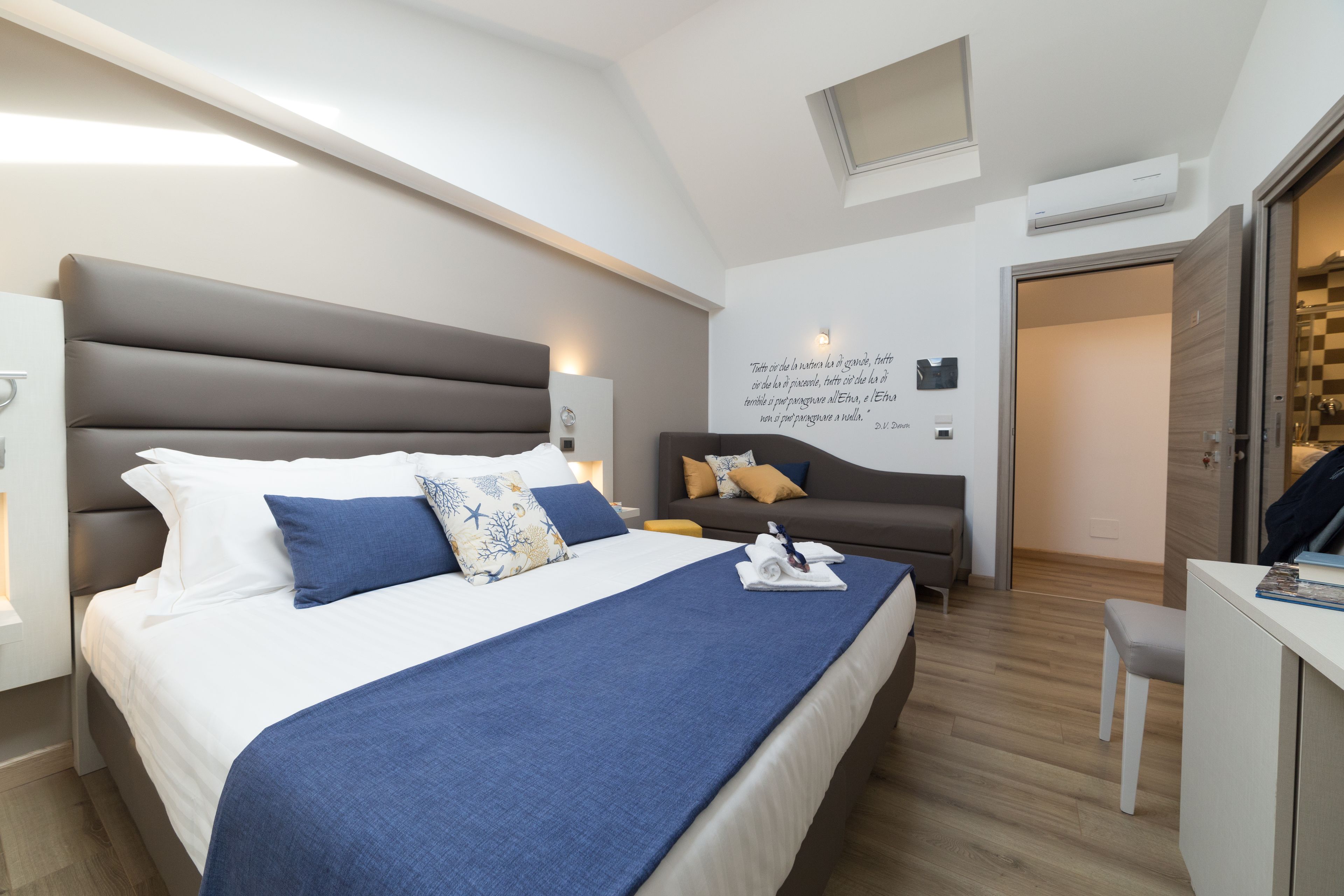 A modern hotel room with a large bed, a desk, and a sofa.