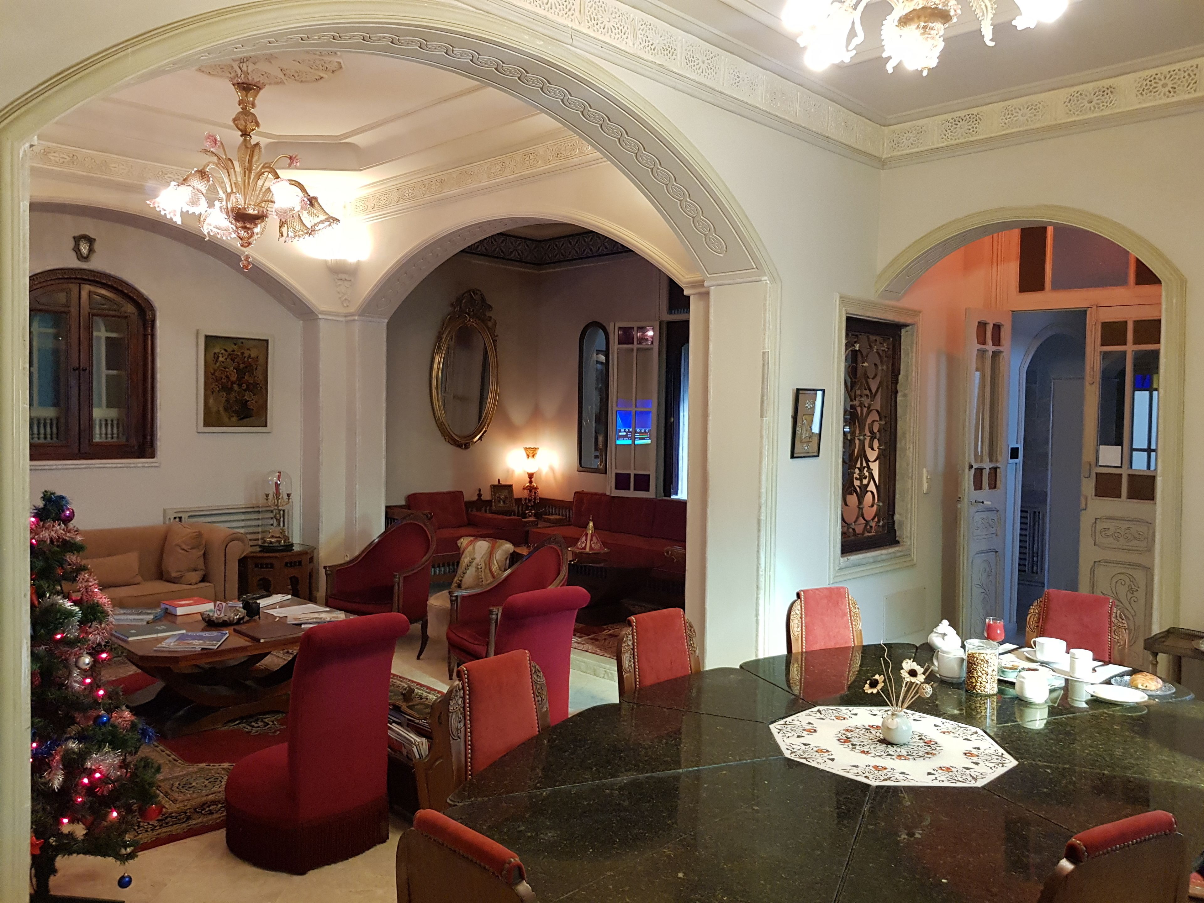 A spacious living room with a large round table, red upholstered chairs, a Christmas tree, and a chandelier.