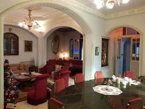 A spacious living room with a large round table, red upholstered chairs, a Christmas tree, and a chandelier. - Dar Ennassim (La Marsa)