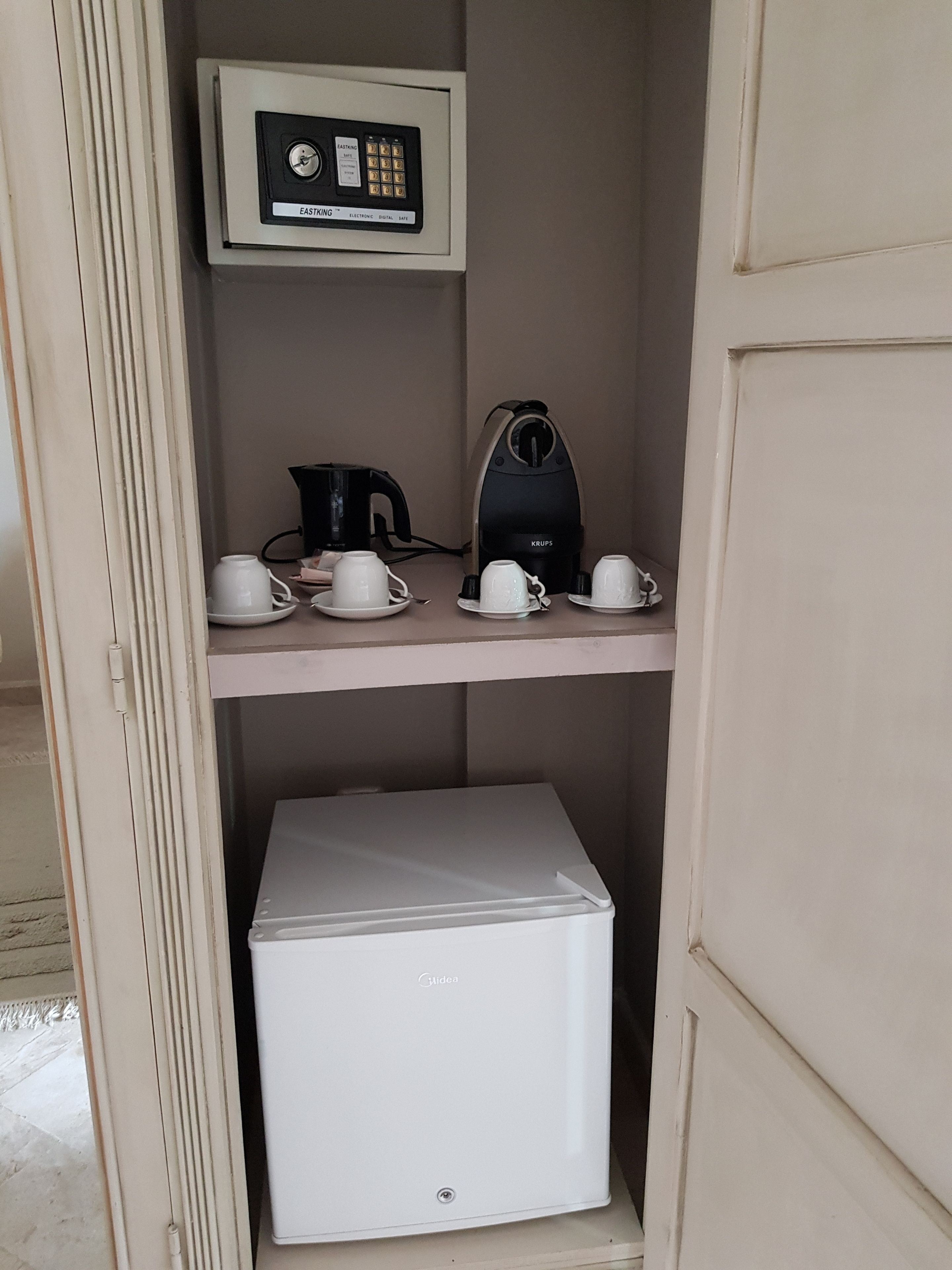 A kitchenette with a coffee maker, cups, a kettle, and a mini-fridge.