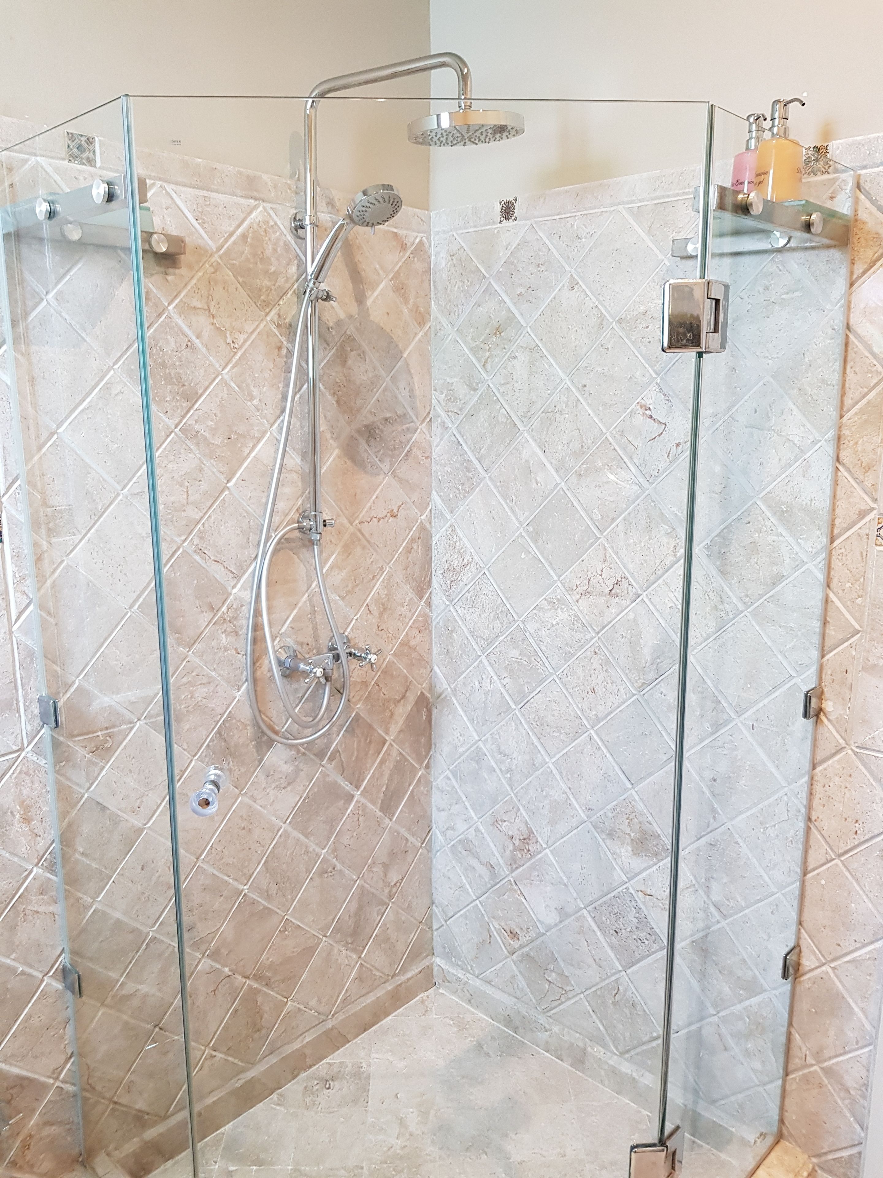 A glass-enclosed shower with a handheld showerhead and a wall-mounted faucet.