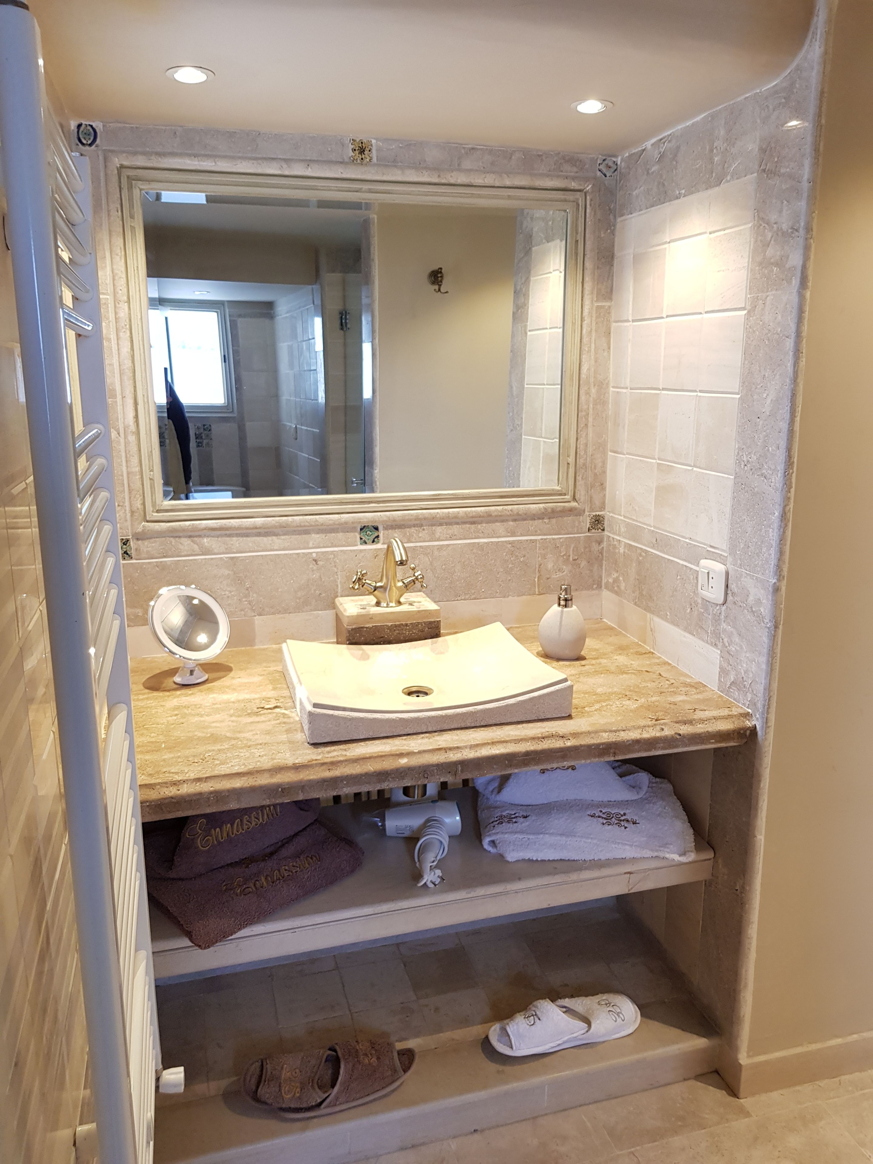 Un baño con un lavabo color beige, un espejo y una ducha a la vista al fondo.