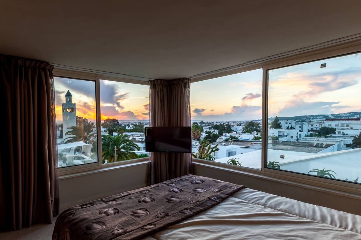 Una habitación de hotel con un ventanal grande, una cama y un televisor de pantalla plana.