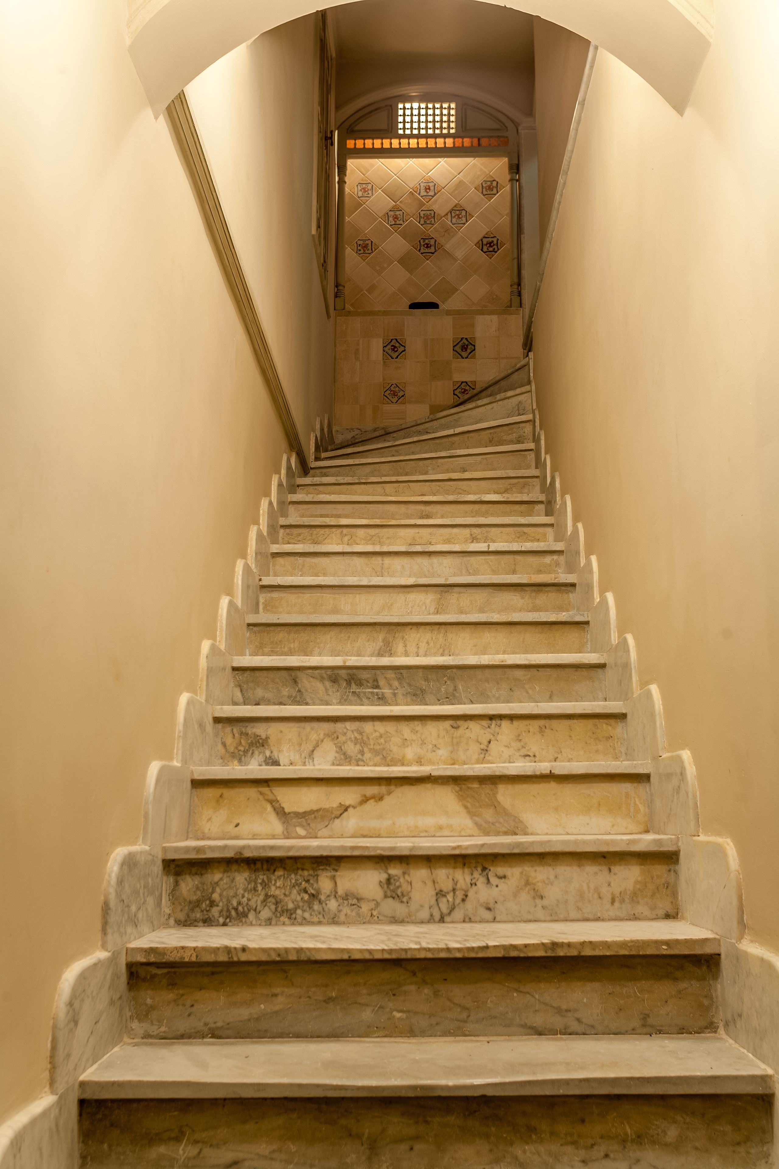 A marble staircase leading to a room with a tiled wall and a window at the top.
