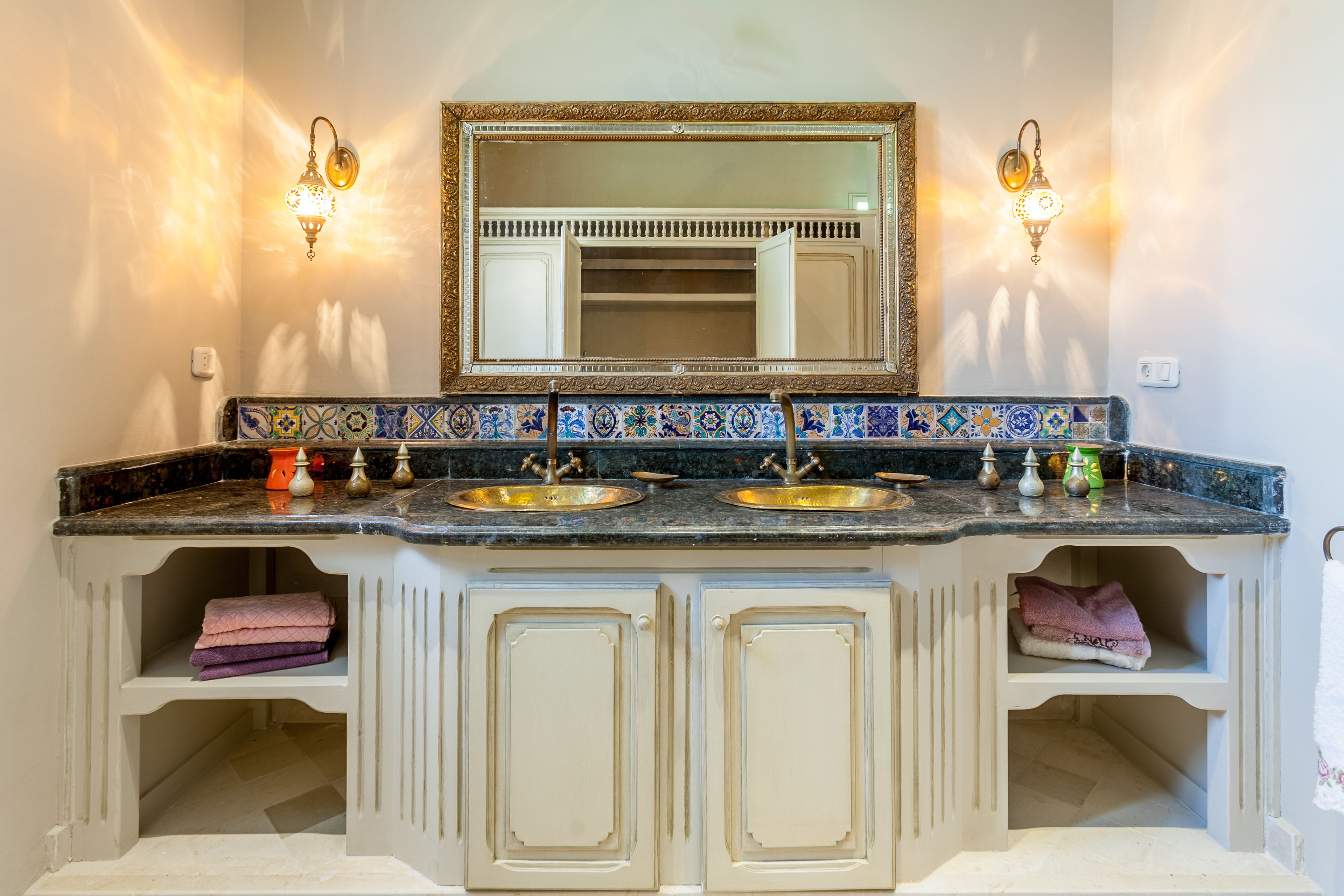 Une salle de bain dotée d’un meuble-lavabo à deux vasques, de deux appliques murales et d’un miroir décoratif.