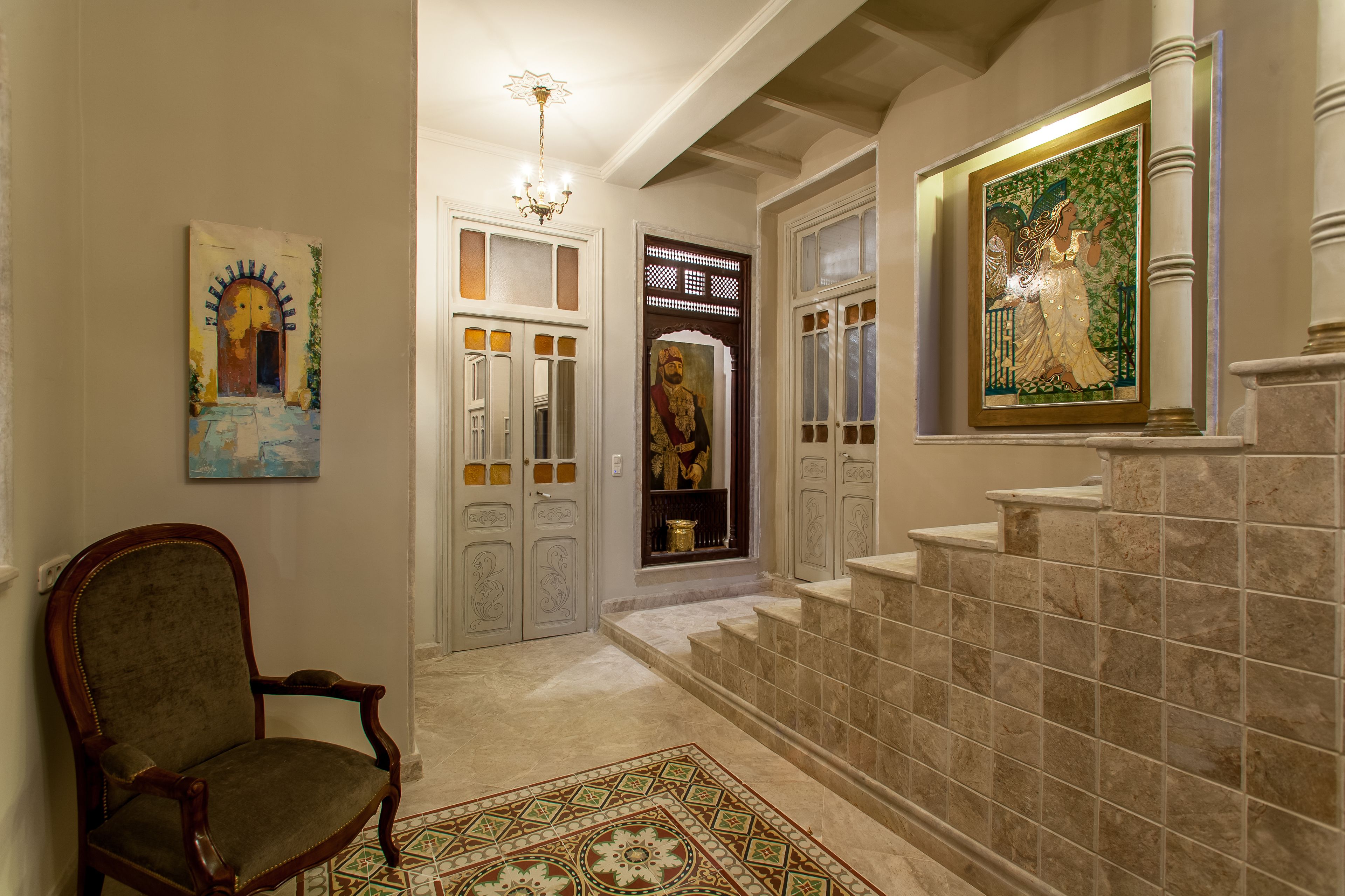 A hallway with a chair, a patterned rug, a staircase, and a framed artwork on the wall.