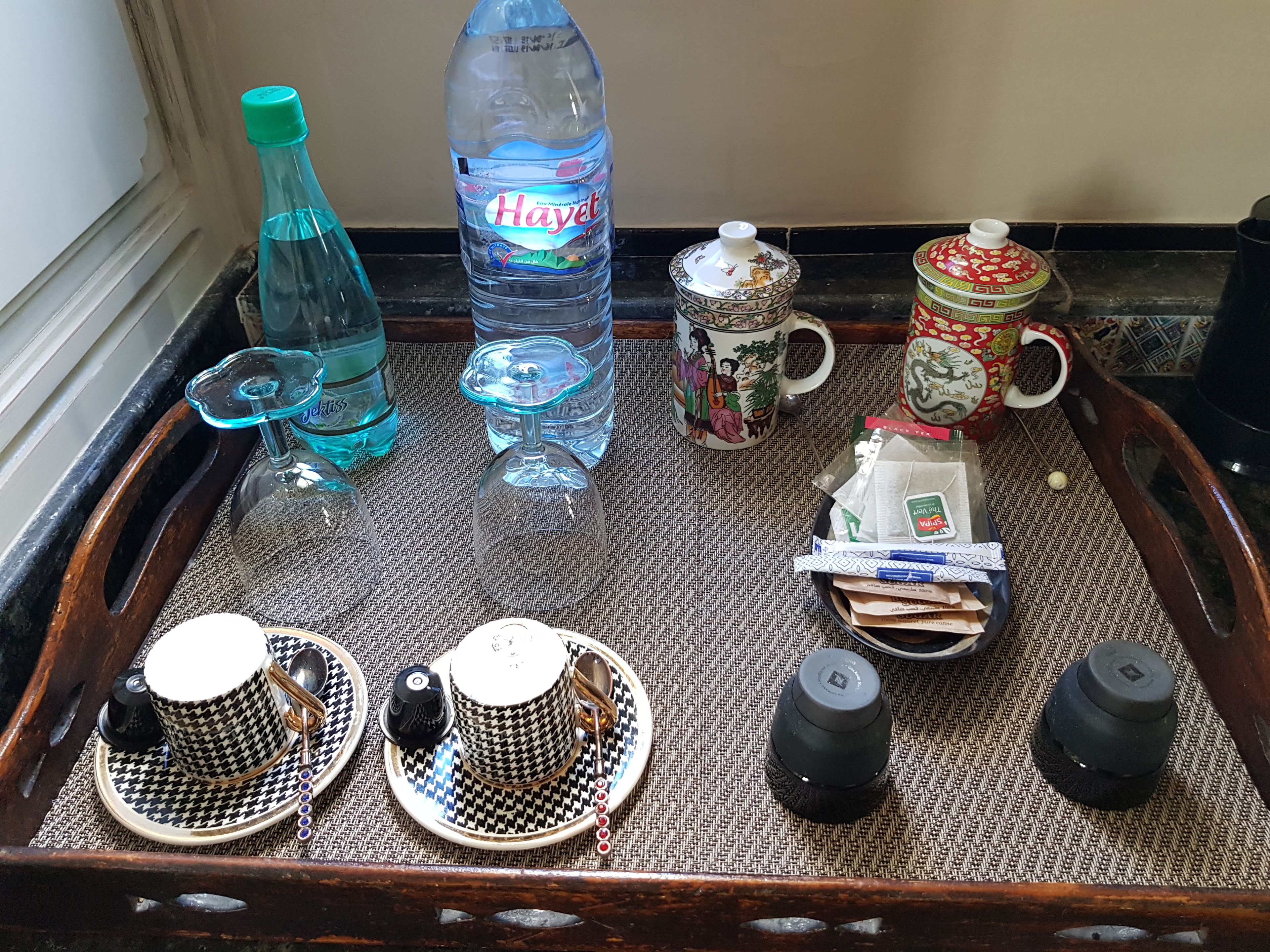 Een dienblad met diverse voorwerpen, waaronder een waterfles, een mok, theekoppen, een theepot en een klein bakje.